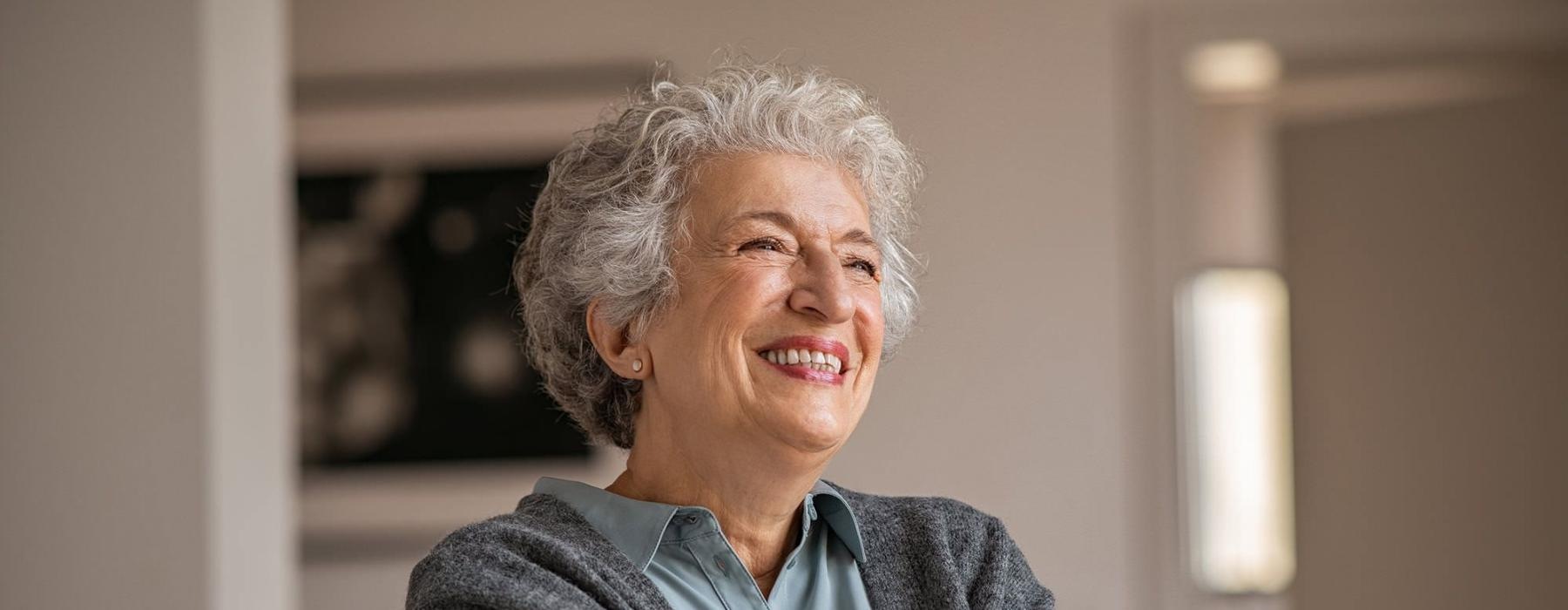 elderly woman with a cane, sits in a room and smiles